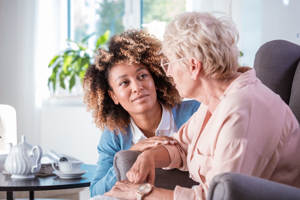 A social worker provides one-on-one comfort to an older patient in a home setting.
