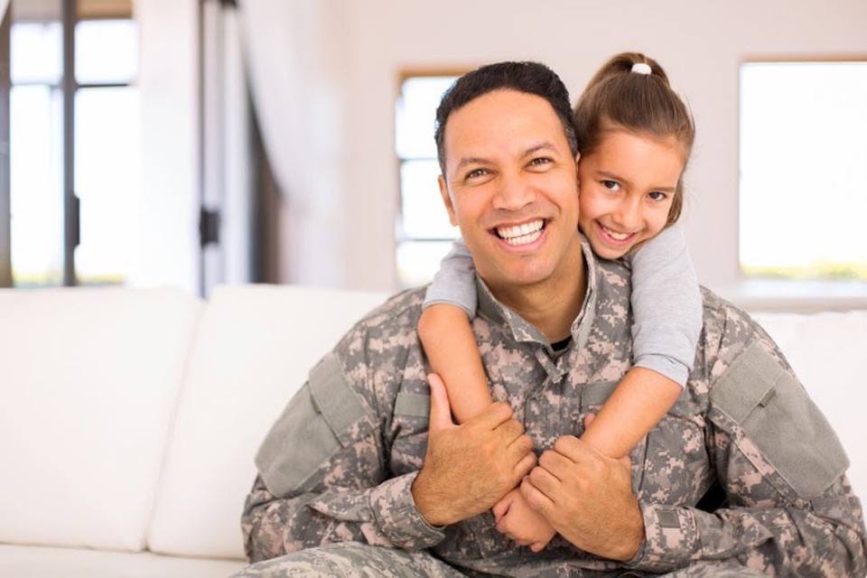 A veteran in a military uniform receives a hug from their young child.
