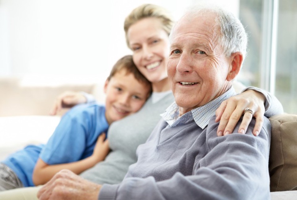 An older person sits on a couch with family members.
