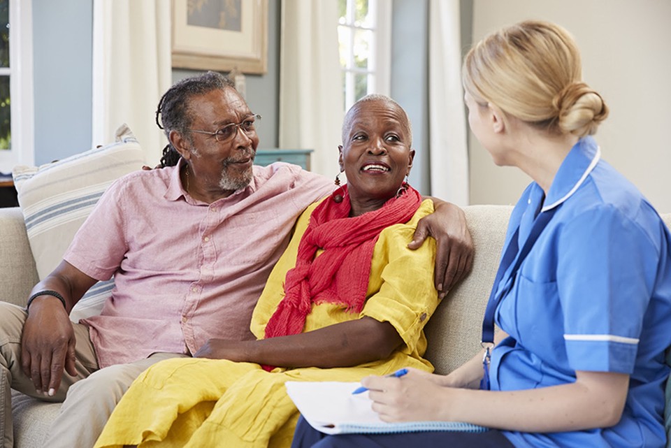A couple sits on a couch and speaks with a health care social worker.