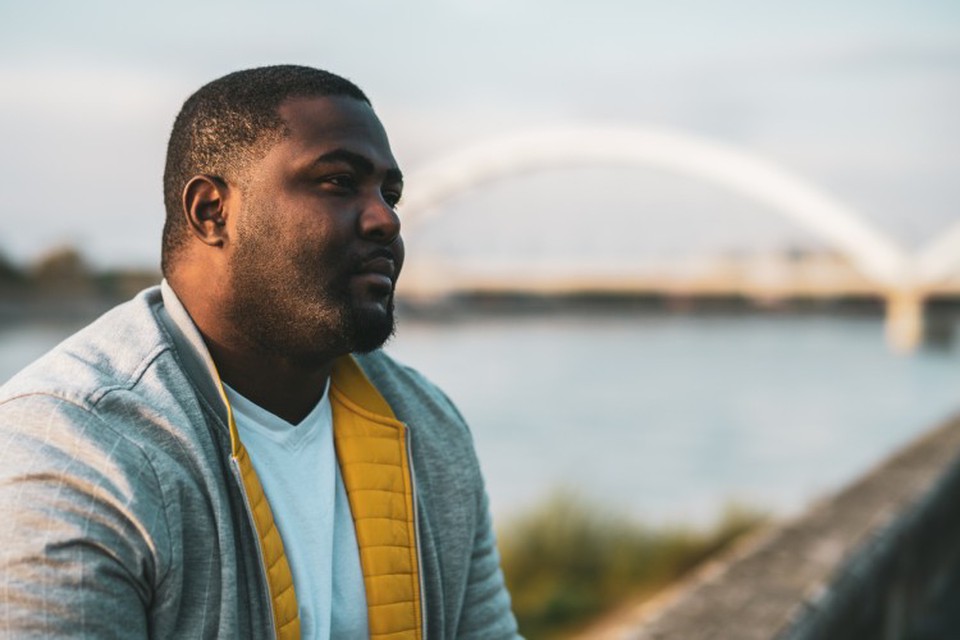 A sad-looking person sits outdoors gazing off into the distance.