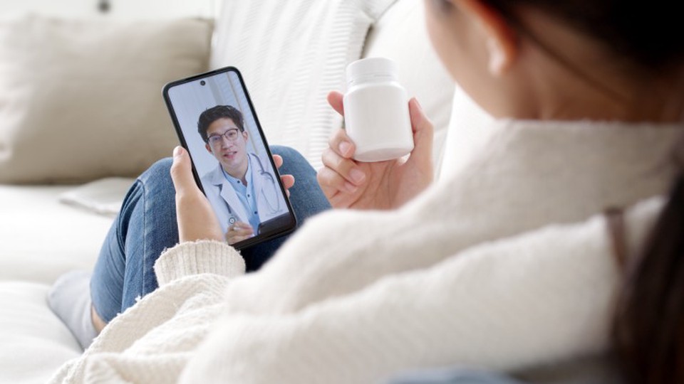 A person holds a prescription bottle while having a telemental health appointment with a provider on a cellphone.