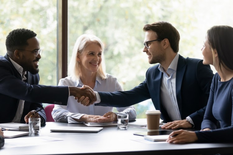 At a meeting, a human resources manager shakes hands with a colleague across a conference table.