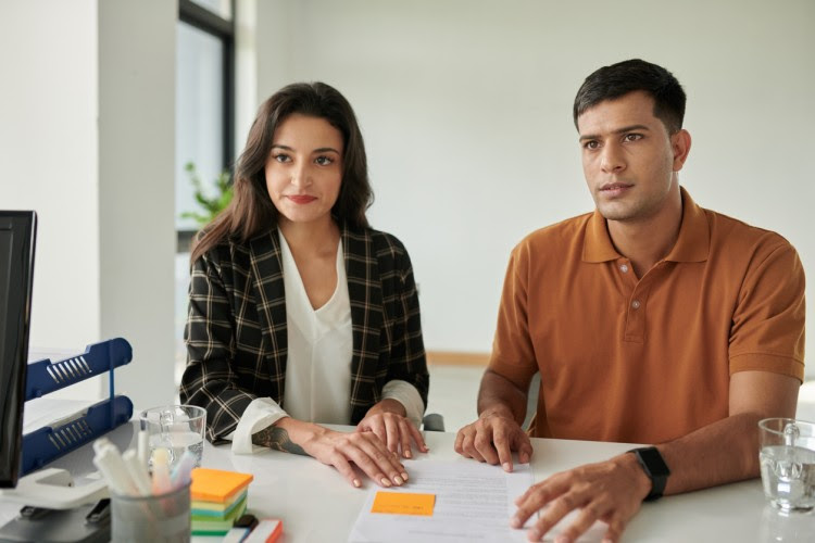 A couple seated side by side at a desk visits a social worker.