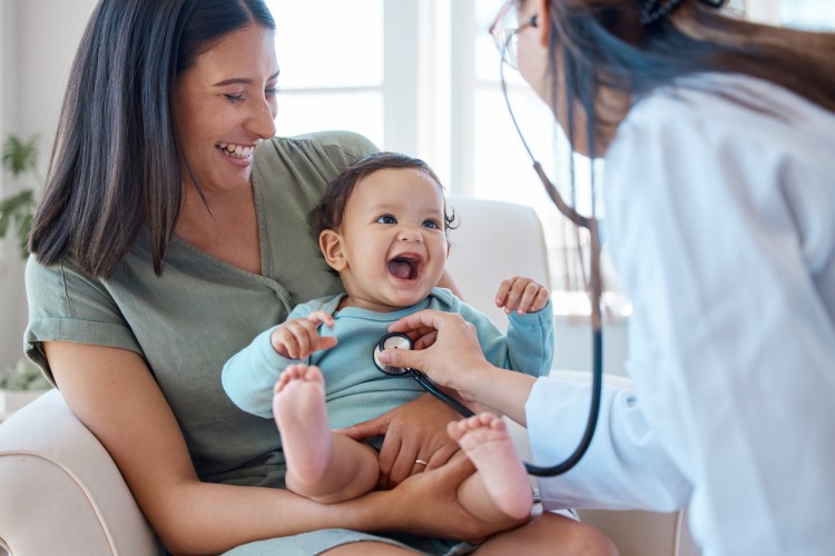 A smiling baby in their parent’s lap is examined by a doctor.