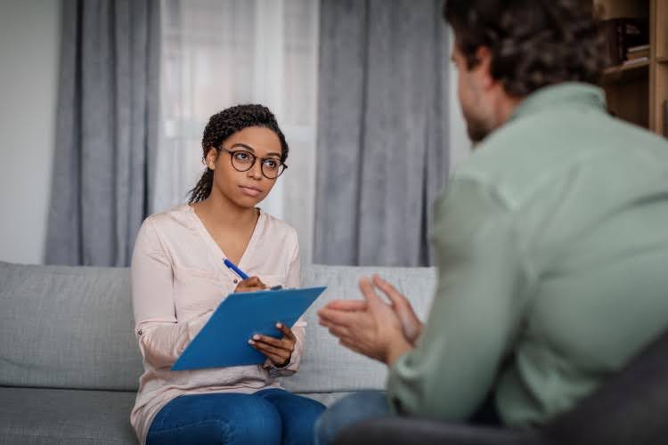 A crisis intervention specialist takes notes on a clipboard while listening to a client.