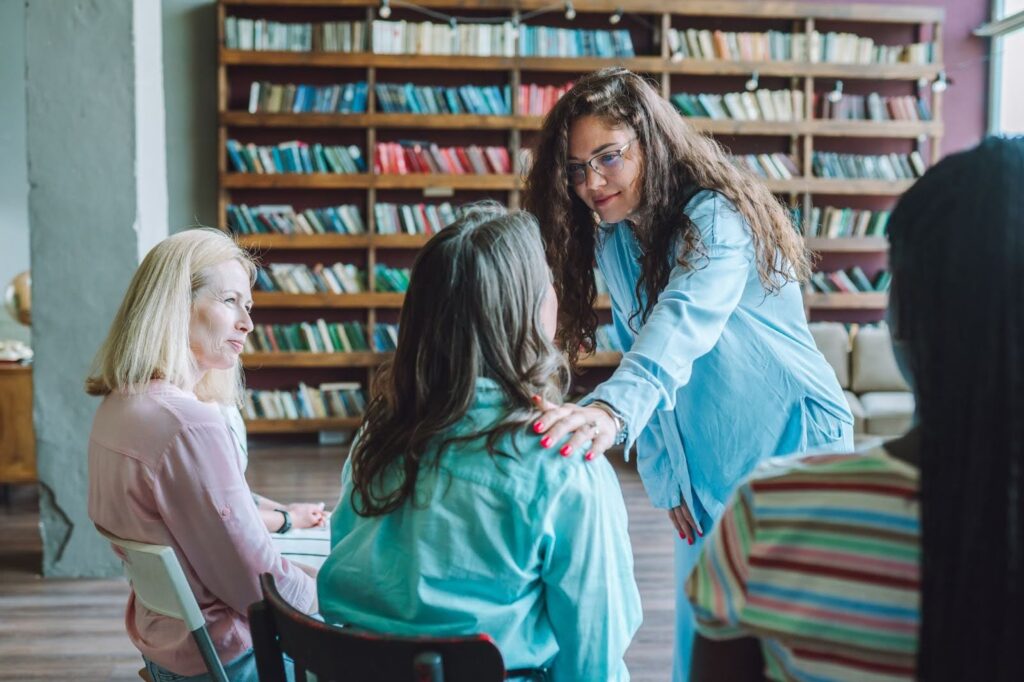A social worker touches a group therapy participant's shoulder to provide emotional support during a session.