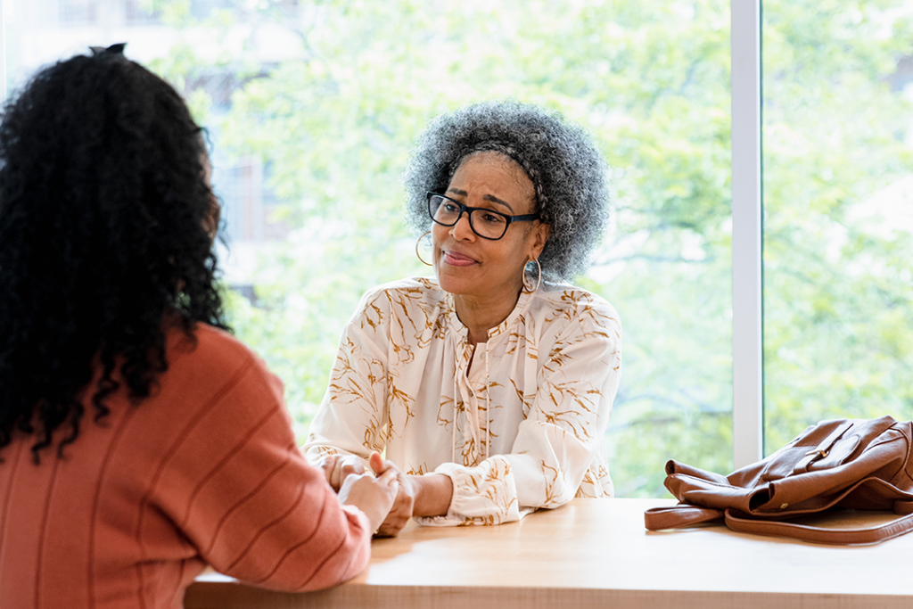 Two people sit at a table, holding hands and engaged in a thoughtful conversation.